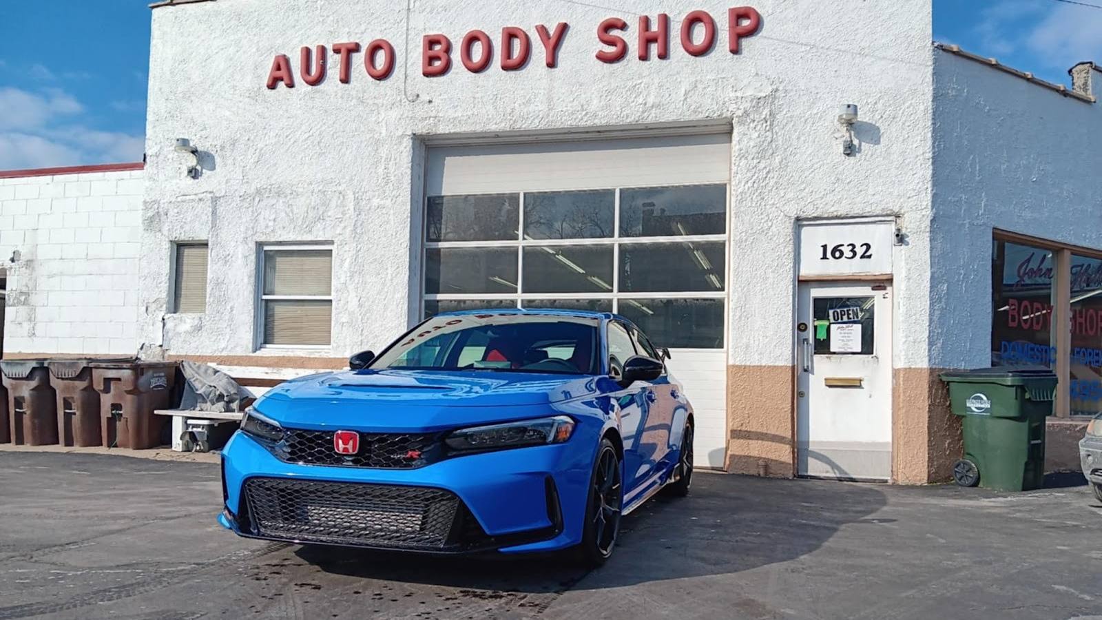 The John Hall Body Shop building at 1632 Hoffner Street, AUTO BODY SHOP lettered in red on white block, with a blue Honda parked at the bay door.