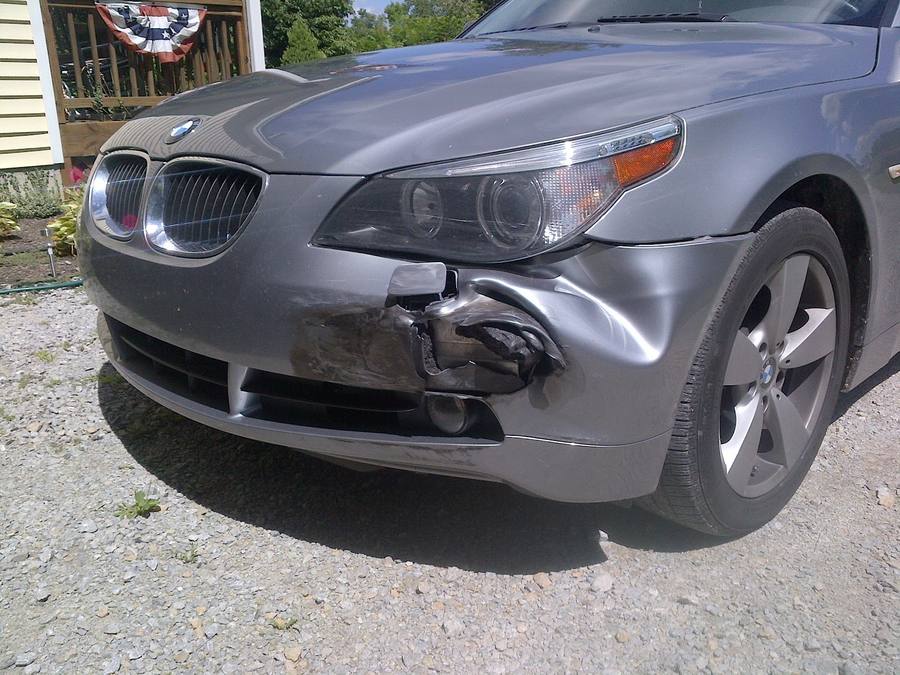 Front-end collision damage to the bumper and headlight of a grey sedan.